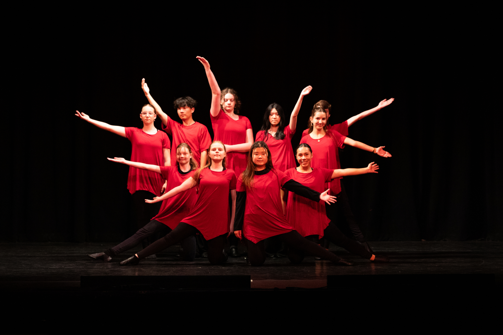Dance students in red posing together at the end of an ensemble piece