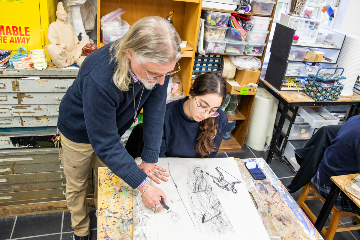 An art teacher works over a student’s charcoal drawing in the studio