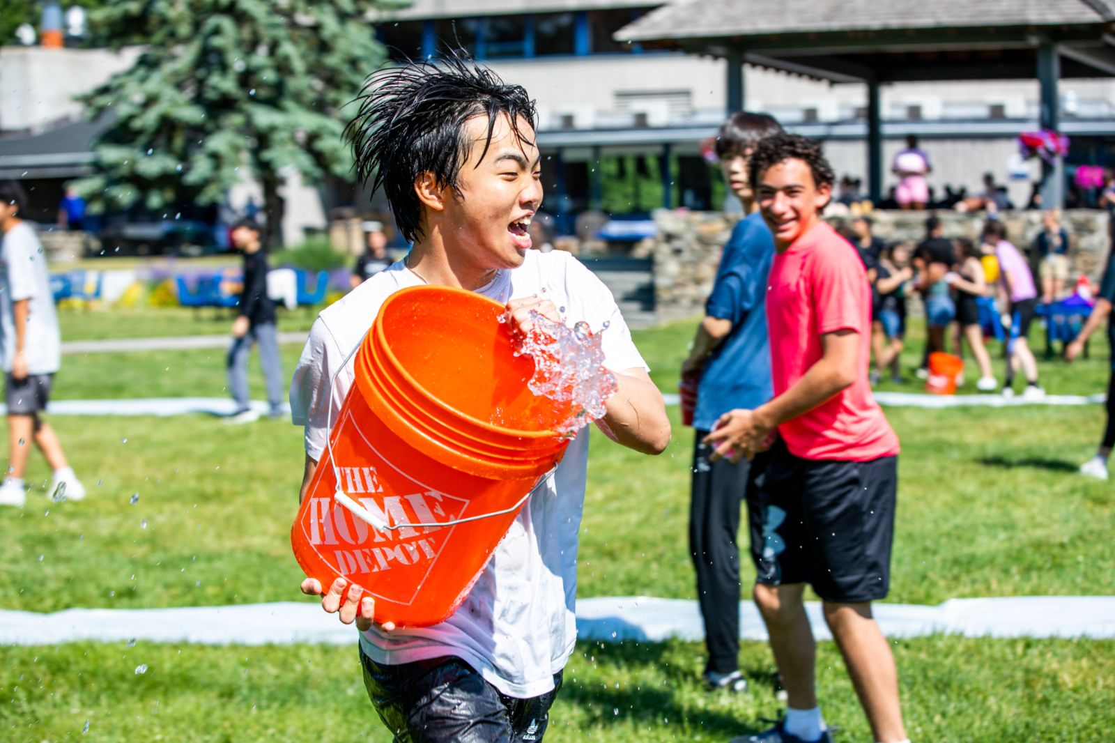 A student doused with water on the campus lawn as classmates laugh