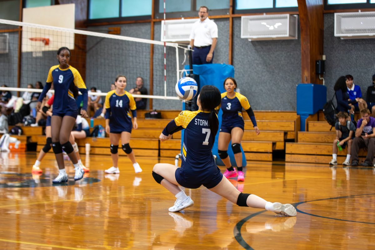 Storm King girls volleyball player stretches low to dig a serve as teammates look on